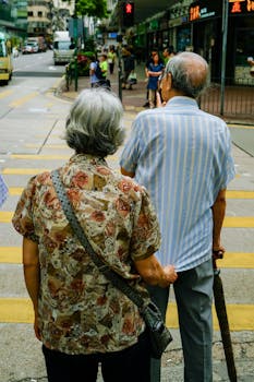 Senior couple waiting at a crosswalk in urban Kowloon, Hong Kong, during the day.